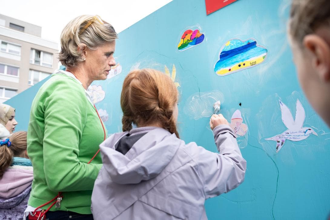 Künstlerin Andrea Wallgren unterstütz eine Schülerin beim Anbringen ihrer Zeichnung auf dem Bauzaun des House of One. 