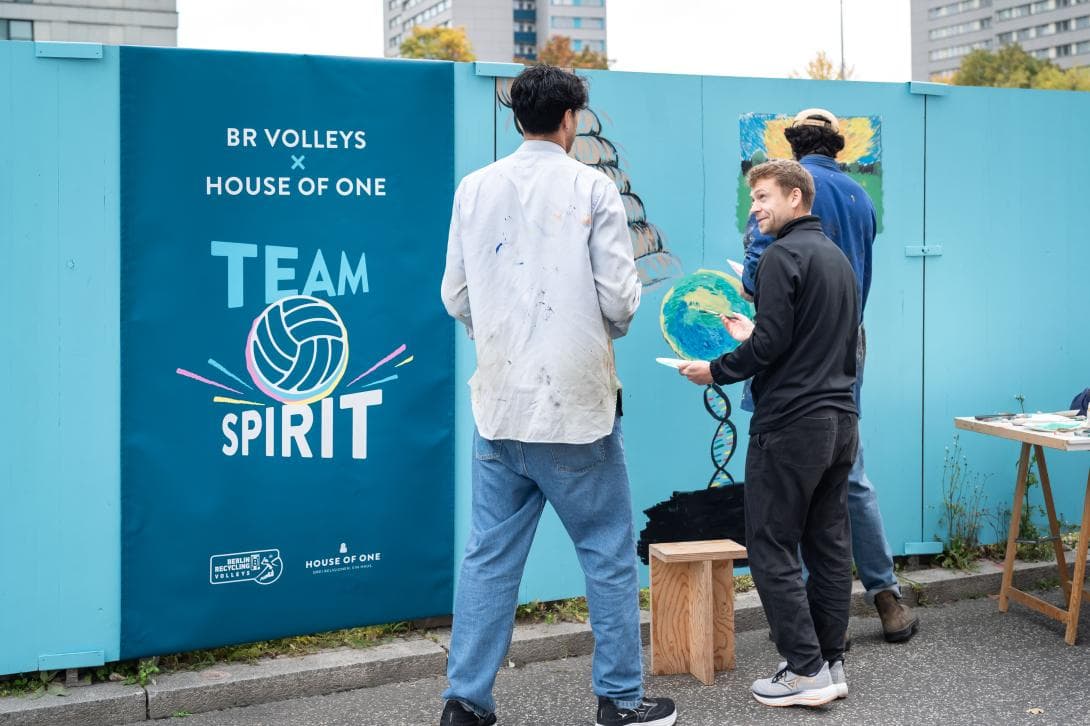 Das Banner mit der Schrift "Team Spirit" als Zeichen der Kooperation von BR Volleys und House of One ist neben der Stelle am Bauzaun aufgehängt, wo die Profis der BR Volleys ihre Friedensbotschaft aufmalen. 